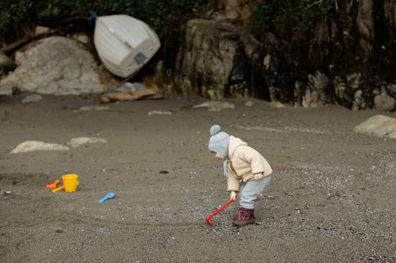 little kid in warm clothes playing with toy shovel on sandy beach